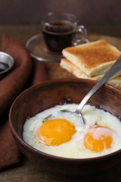 Photo of Half-boiled eggs in bowl, coffee and toasted bread on wooden table, closeup