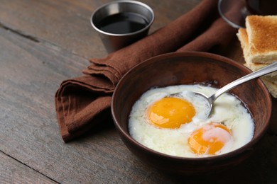 Photo of Half-boiled eggs in bowl, soy sauce and toasted bread on wooden table, closeup. Space for text