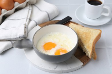 Photo of Half-boiled eggs in bowl, coffee and toasted bread on white tiled table, closeup