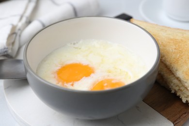 Photo of Half-boiled eggs in bowl and toasted bread on white tiled table, closeup