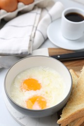 Photo of Half-boiled eggs in bowl, coffee and toasted bread on white tiled table, closeup