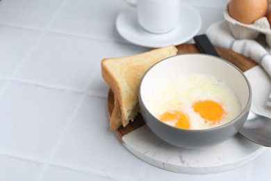 Photo of Half-boiled eggs in bowl and toasted bread on white tiled table, closeup. Space for text