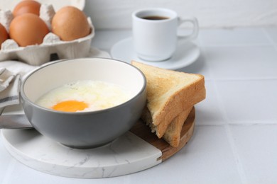 Photo of Half-boiled eggs in bowl, coffee and toasted bread on white tiled table, closeup. Space for text