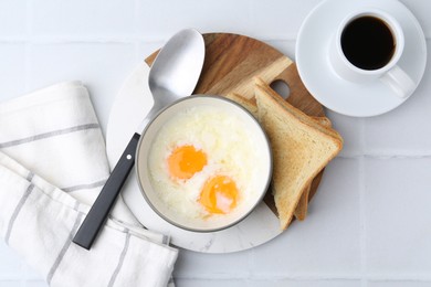 Photo of Half-boiled eggs in bowl, coffee and toasted bread on white tiled table, flat lay