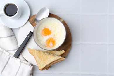 Photo of Half-boiled eggs in bowl, coffee and toasted bread on white tiled table, flat lay. Space for text
