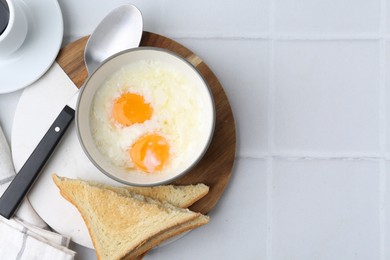 Photo of Half-boiled eggs in bowl, coffee and toasted bread on white tiled table, flat lay. Space for text