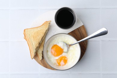 Photo of Half-boiled eggs in bowl, soy sauce and toasted bread on white tiled table, flat lay
