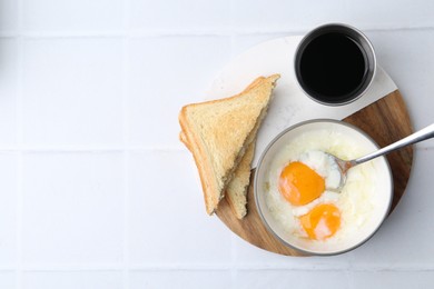 Photo of Half-boiled eggs in bowl, soy sauce and toasted bread on white tiled table, flat lay. Space for text