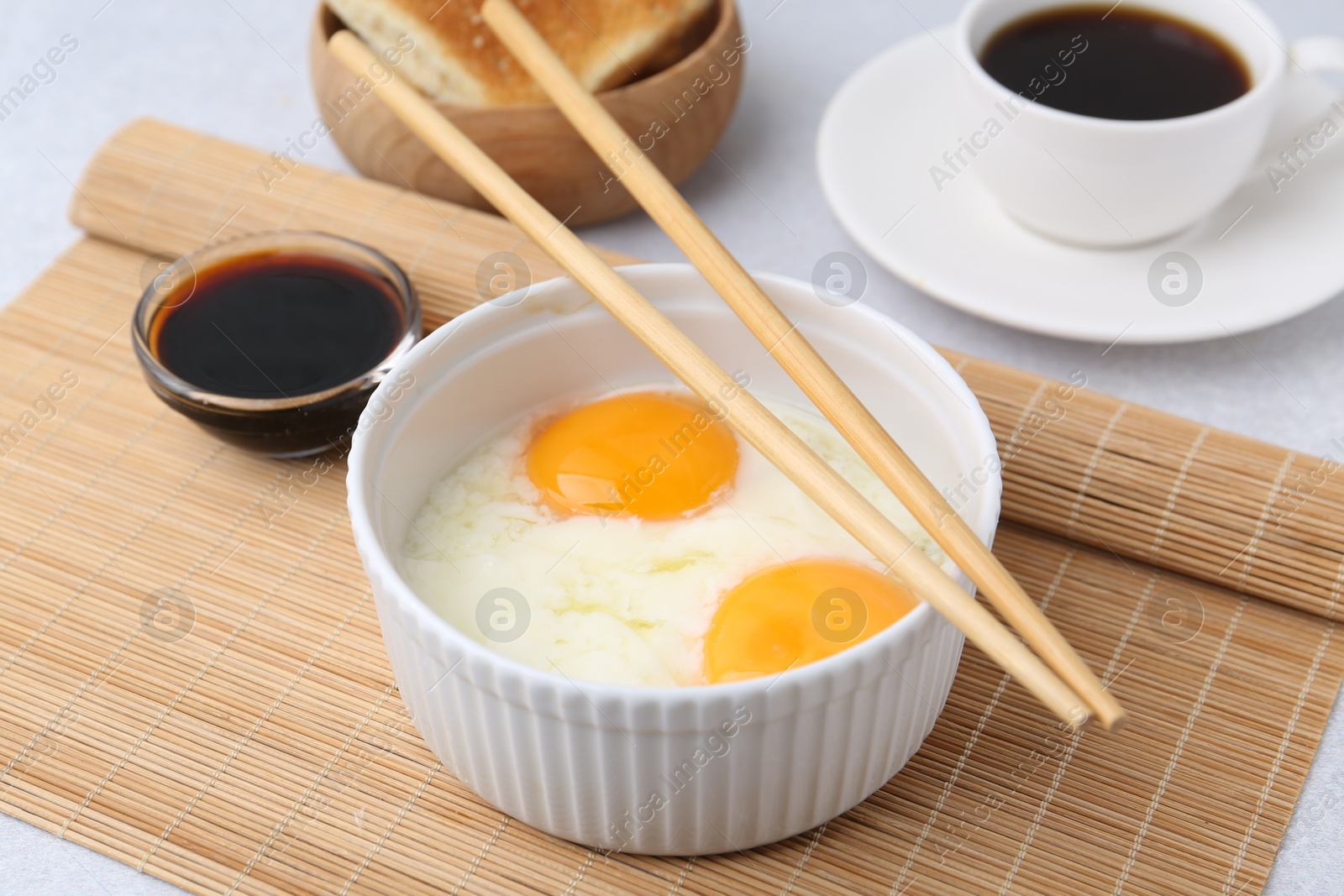 Half-boiled eggs in bowl, soy sauce, chopsticks, coffee and toasted bread on light grey table, closeup Photo of Half-boiled eggs in bowl, soy sauce, chopsticks, coffee and toasted bread on light grey table, closeup