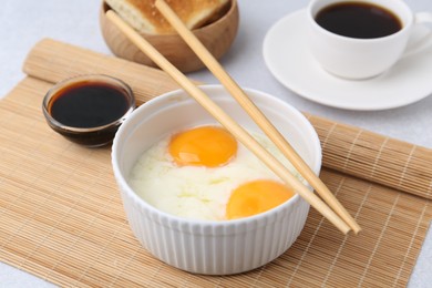 Photo of Half-boiled eggs in bowl, soy sauce, chopsticks, coffee and toasted bread on light grey table, closeup