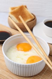 Photo of Half-boiled eggs in bowl, soy sauce, chopsticks, coffee and toasted bread on light grey table, closeup