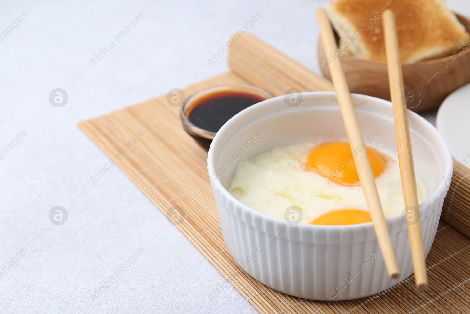Half-boiled eggs in bowl, soy sauce, chopsticks and toasted bread on light grey table, closeup. Space for text Photo of Half-boiled eggs in bowl, soy sauce, chopsticks and toasted bread on light grey table, closeup. Space for text
