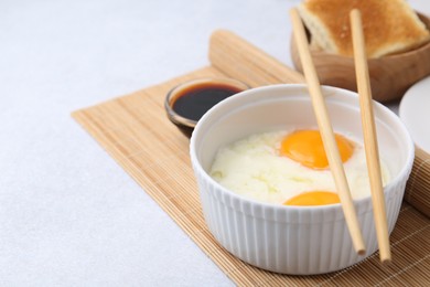 Photo of Half-boiled eggs in bowl, soy sauce, chopsticks and toasted bread on light grey table, closeup. Space for text