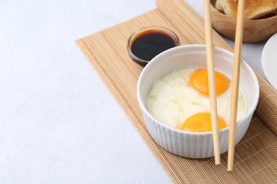 Photo of Half-boiled eggs in bowl, soy sauce, chopsticks and toasted bread on light grey table, closeup. Space for text