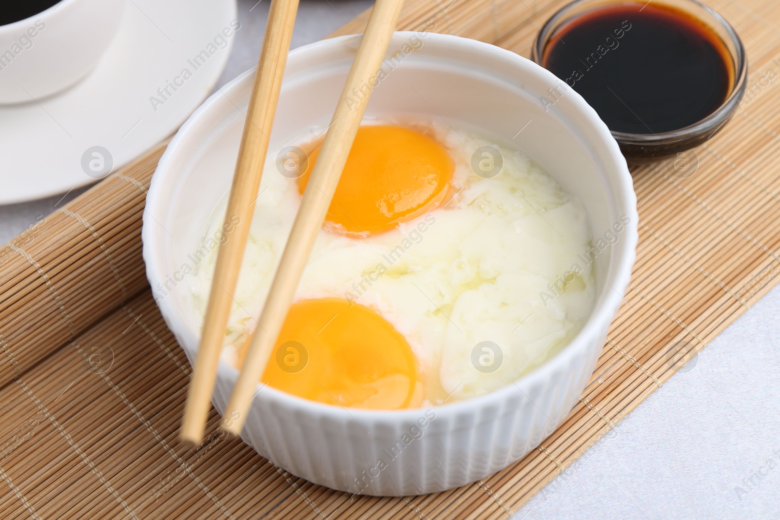 Half-boiled eggs in bowl, soy sauce and chopsticks on light grey table, closeup Photo of Half-boiled eggs in bowl, soy sauce and chopsticks on light grey table, closeup