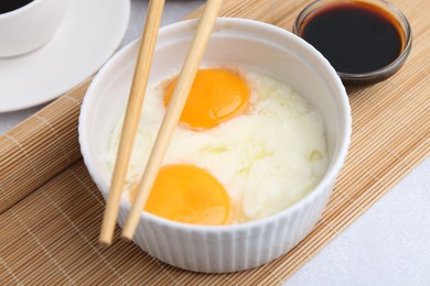 Photo of Half-boiled eggs in bowl, soy sauce and chopsticks on light grey table, closeup