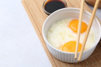 Photo of Half-boiled eggs in bowl, soy sauce and chopsticks on light grey table, closeup. Space for text