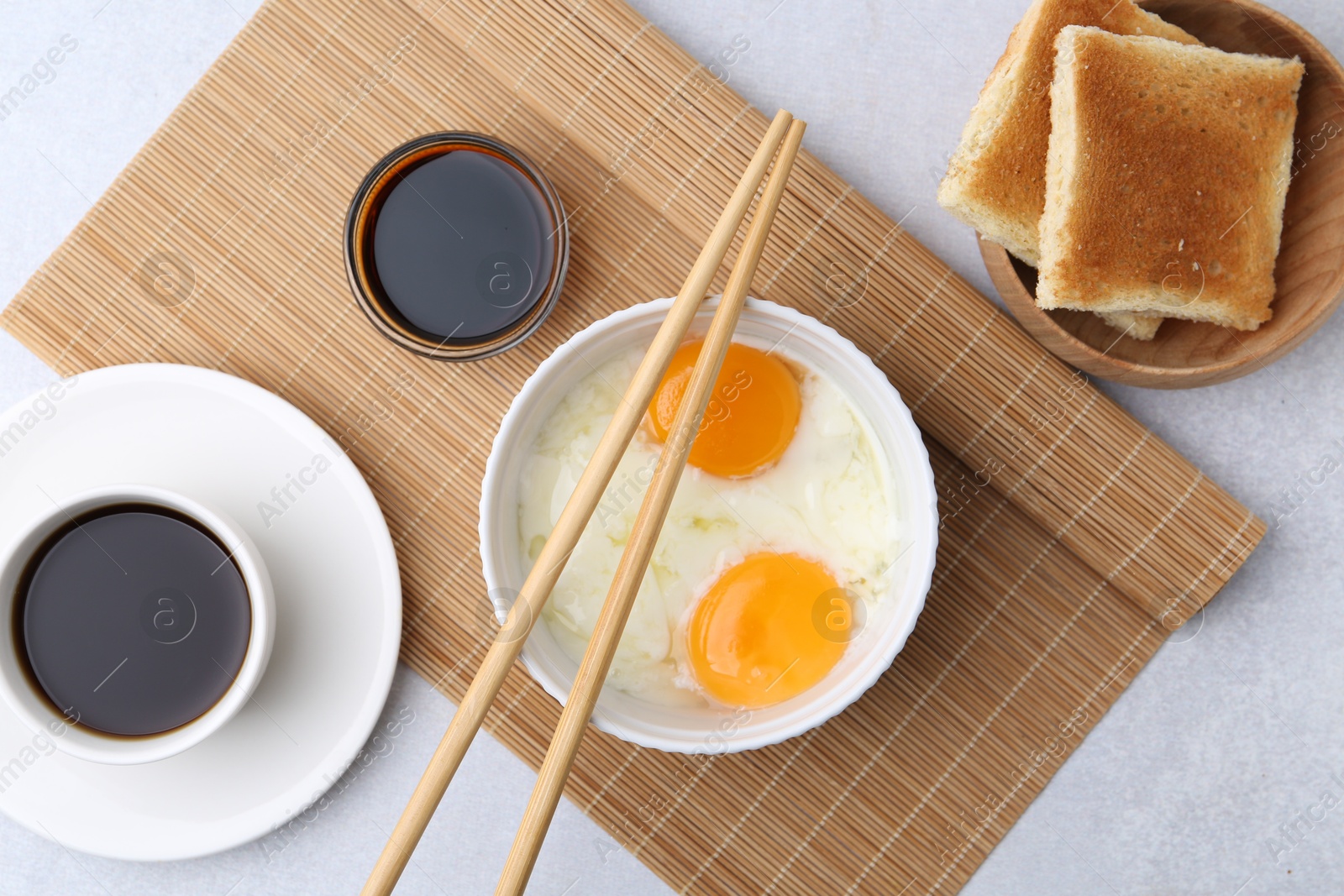 Half-boiled eggs in bowl, soy sauce, chopsticks, coffee and toasted bread on light grey table, flat lay Photo of Half-boiled eggs in bowl, soy sauce, chopsticks, coffee and toasted bread on light grey table, flat lay