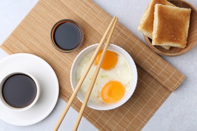 Photo of Half-boiled eggs in bowl, soy sauce, chopsticks, coffee and toasted bread on light grey table, flat lay