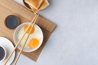 Photo of Half-boiled eggs, soy sauce, chopsticks, coffee and toasted bread on light grey table, flat lay. Space for text