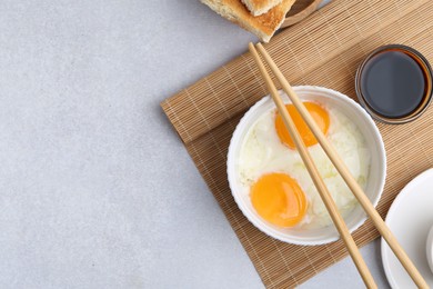 Photo of Half-boiled eggs in bowl, soy sauce, chopsticks and toasted bread on light grey table, flat lay. Space for text