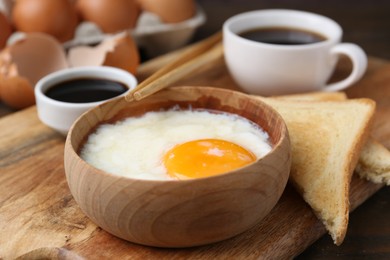 Photo of Half-boiled egg in bowl, soy sauce, chopsticks, coffee and toasted bread on table, closeup
