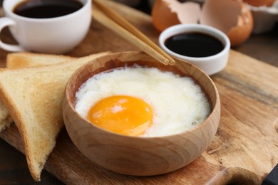 Photo of Half-boiled egg in bowl, soy sauce, chopsticks, coffee and toasted bread on table, closeup