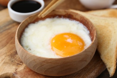 Photo of Half-boiled egg in bowl, soy sauce, chopsticks and toasted bread on table, closeup