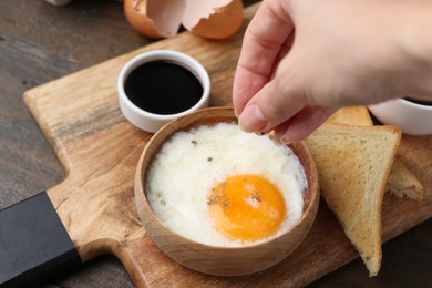 Photo of Woman putting spices onto half-boiled egg at wooden table, closeup