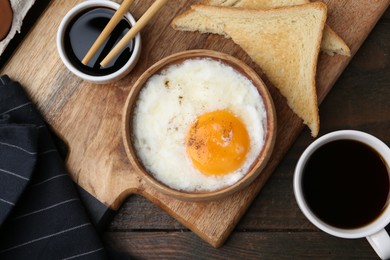 Photo of Half-boiled egg in bowl, soy sauce, chopsticks, coffee and toasted bread on wooden table, flat lay