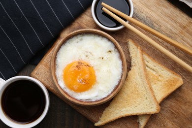 Photo of Half-boiled egg in bowl, soy sauce, chopsticks, coffee and toasted bread on wooden table, flat lay