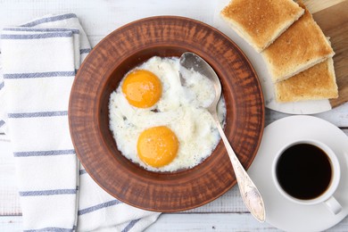 Photo of Half-boiled eggs in plate, coffee and toasted bread on white wooden table, flat lay