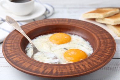 Photo of Half-boiled eggs in plate, spoon and toasted bread on white wooden table, closeup