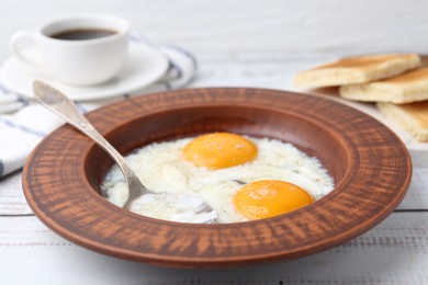Photo of Half-boiled eggs in plate, spoon and toasted bread on white wooden table, closeup