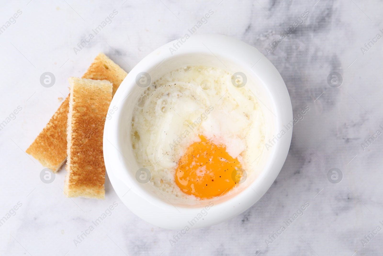 Half-boiled egg in bowl and toasted bread on white marble table, top view Photo of Half-boiled egg in bowl and toasted bread on white marble table, top view