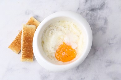Photo of Half-boiled egg in bowl and toasted bread on white marble table, top view