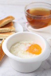 Photo of Half-boiled egg in bowl and toasted bread on white marble table, closeup