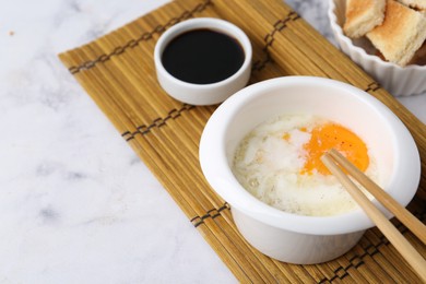 Photo of Half-boiled egg in bowl, soy sauce, chopsticks and toasted bread on white marble table, closeup. Space for text