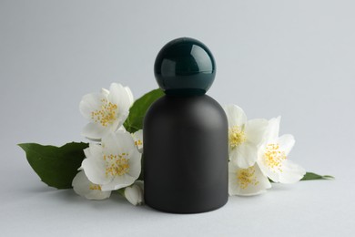 Photo of Bottle of perfume and jasmine flowers on light background, closeup
