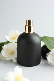 Photo of Bottle of perfume and jasmine flowers on light background, closeup