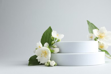 Photo of Beautiful jasmine flowers with leaves on light background. Space for text