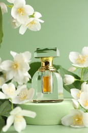 Photo of Bottle of perfume and jasmine flowers on green background, closeup