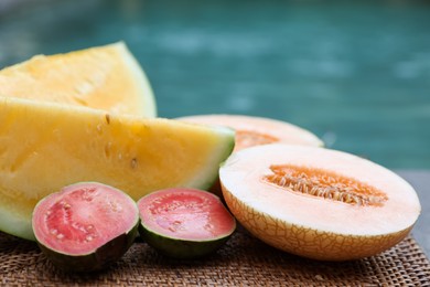 Photo of Ripe juicy tropical fruits on wicker tray near swimming pool, closeup