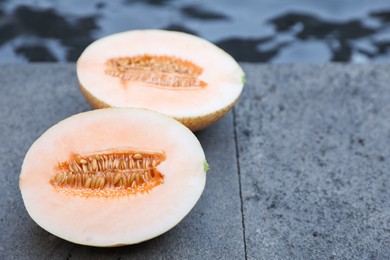 Photo of Halves of juicy melon on grey surface near swimming pool, closeup. Space for text