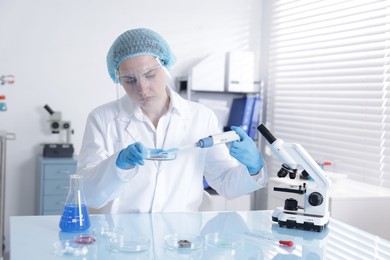 Photo of Scientist working with sample in Petri dish at table in laboratory