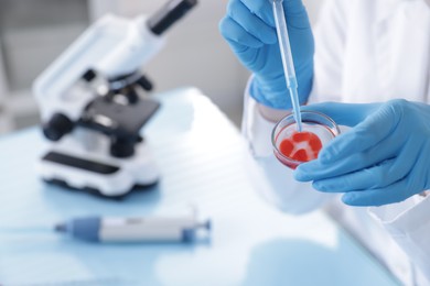 Photo of Scientist working with sample in Petri dish at table in laboratory, closeup