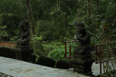 Photo of Bali, Indonesia - May 24, 2025: Beautiful ancient statues and different green plants outdoors