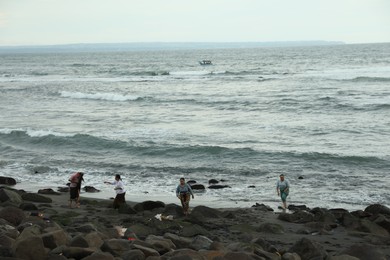 Photo of Bali, Indonesia - May 27, 2025: People resting on rocky beach near sea