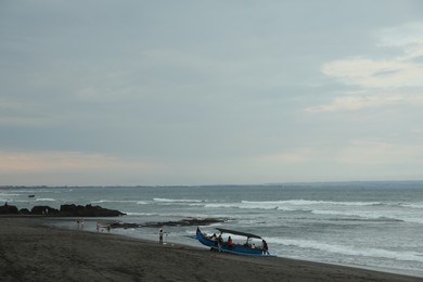Photo of Bali, Indonesia - May 27, 2025: View of sandy beach, people, boat and wavy sea under blue sky
