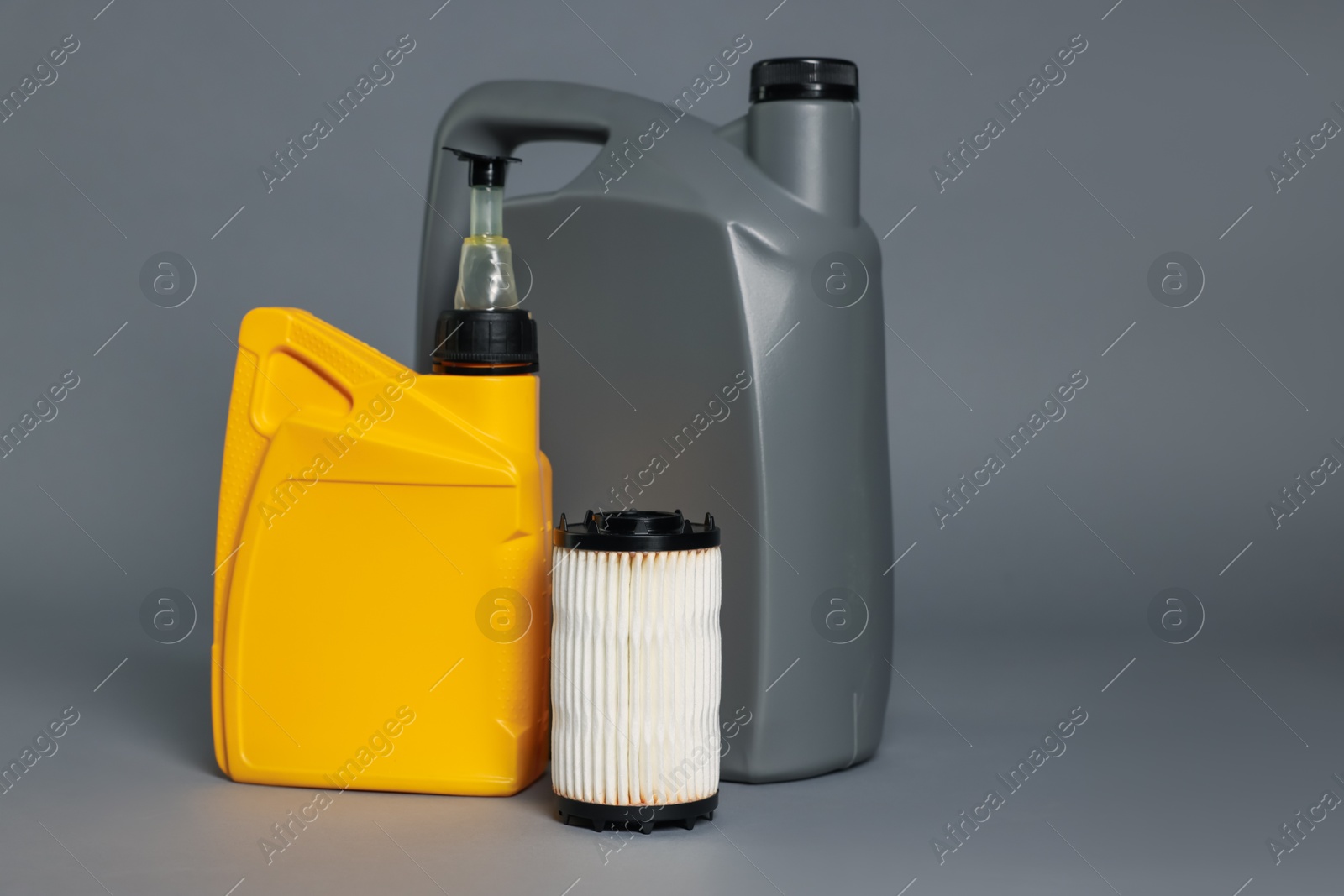 Photo of Motor oil in plastic canisters and filter on grey background, space for text